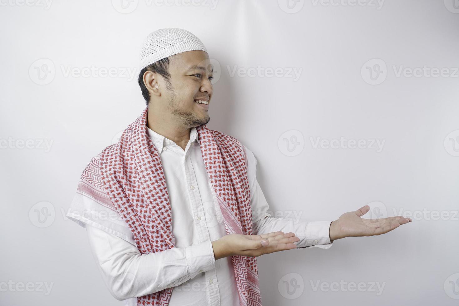 Excited Asian Muslim man pointing at the copy space beside him, isolated by white background photo