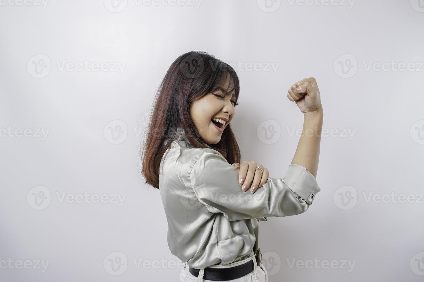 mujer asiática emocionada con una camisa verde salvia que muestra un gesto fuerte levantando los brazos y los músculos sonriendo con orgullo foto