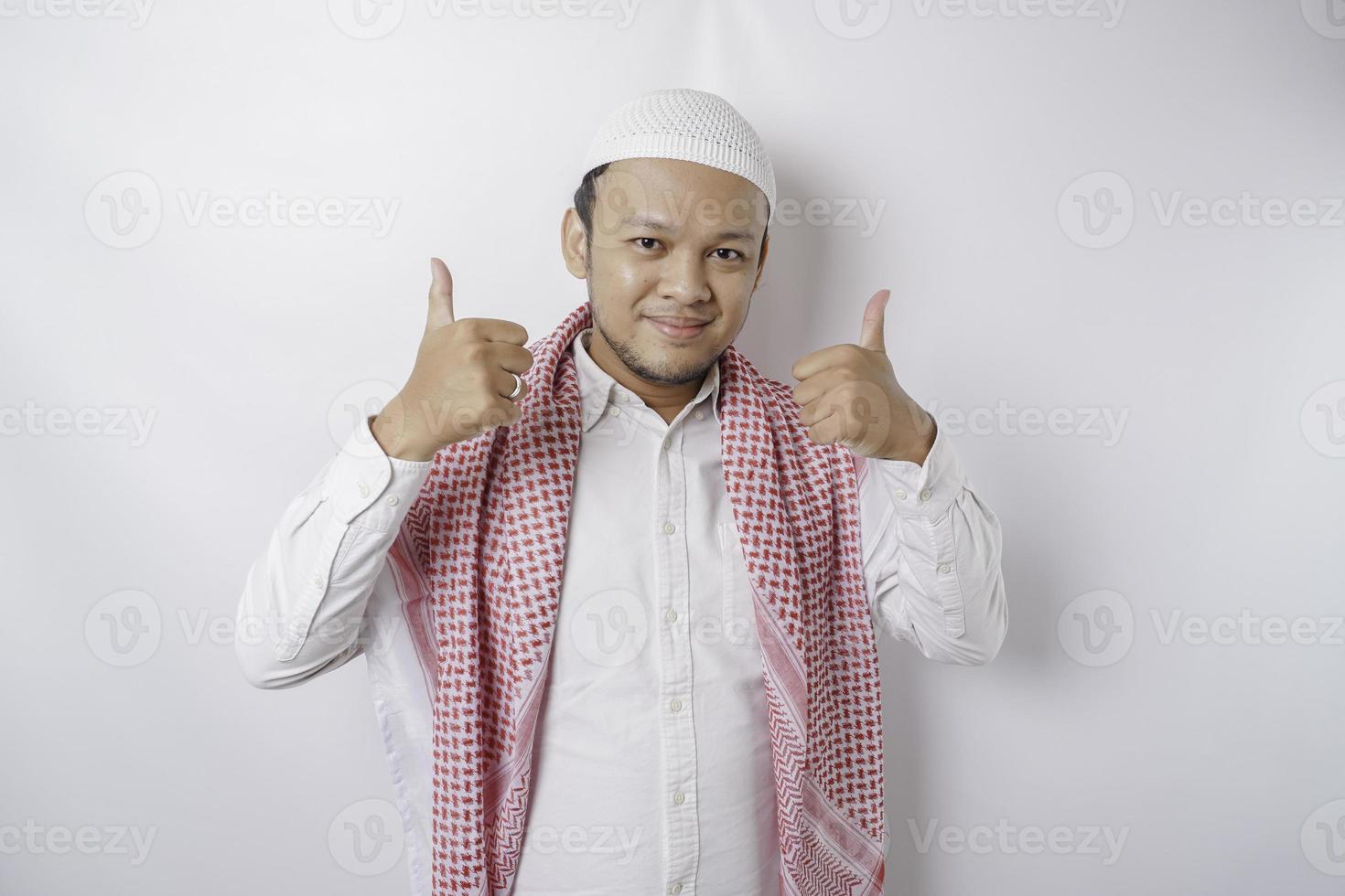 Excited Asian Muslim man gives thumbs up hand gesture of approval, isolated by white background photo