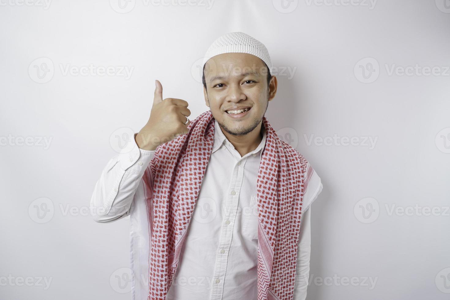 Excited Asian Muslim man gives thumbs up hand gesture of approval, isolated by white background photo