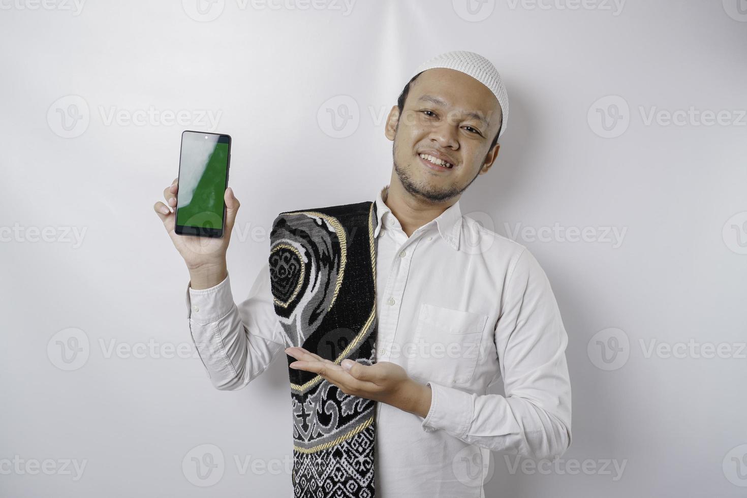 un retrato de un musulmán asiático feliz sonriendo mientras muestra espacio de copia en su teléfono, aislado por fondo blanco foto