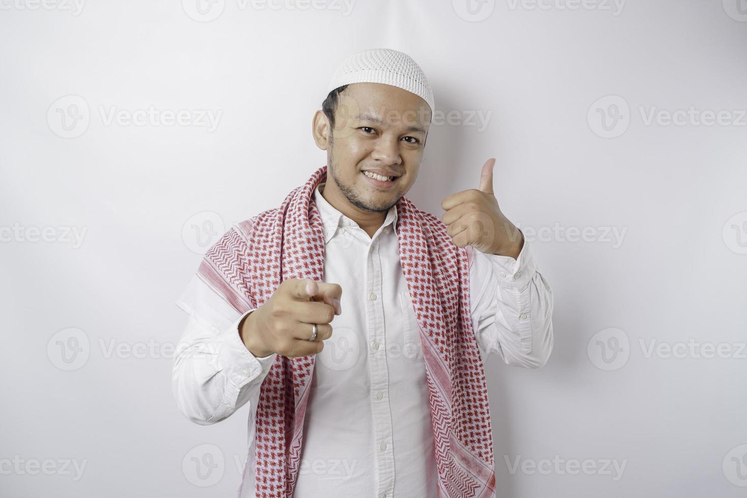 Excited Asian Muslim man gives thumbs up hand gesture of approval, isolated by white background photo