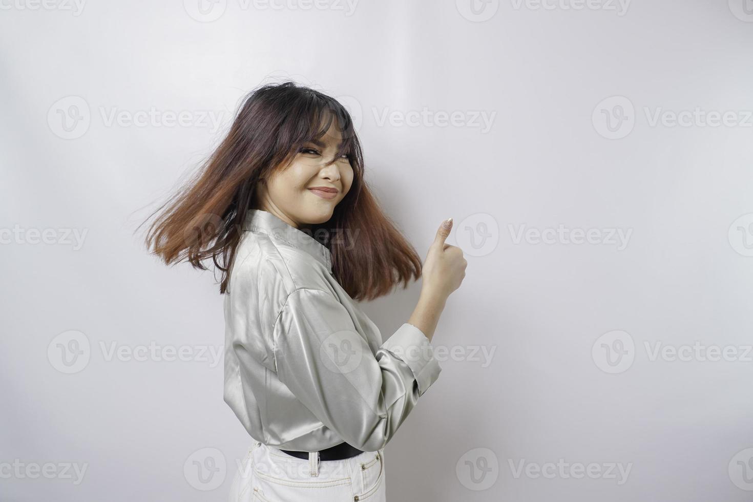 Excited Asian woman wearing sage green shirt gives thumbs up hand gesture of approval, isolated by white background photo