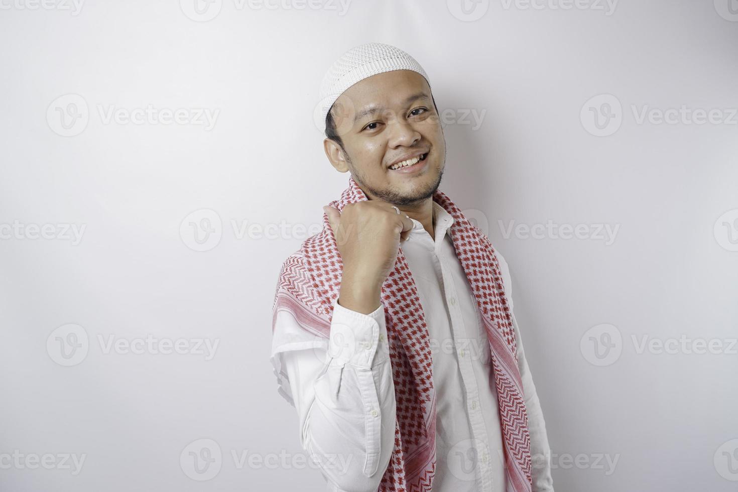 Excited Asian Muslim man pointing at the copy space beside him, isolated by white background photo