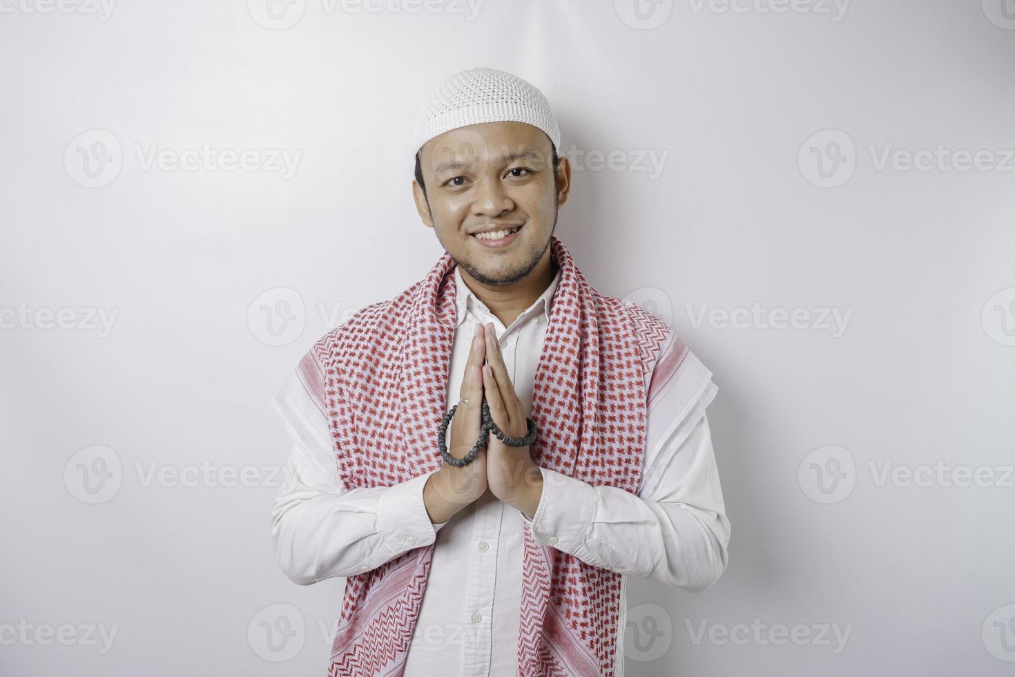 Smiling young Asian Muslim man, gesturing traditional greeting isolated over white background photo