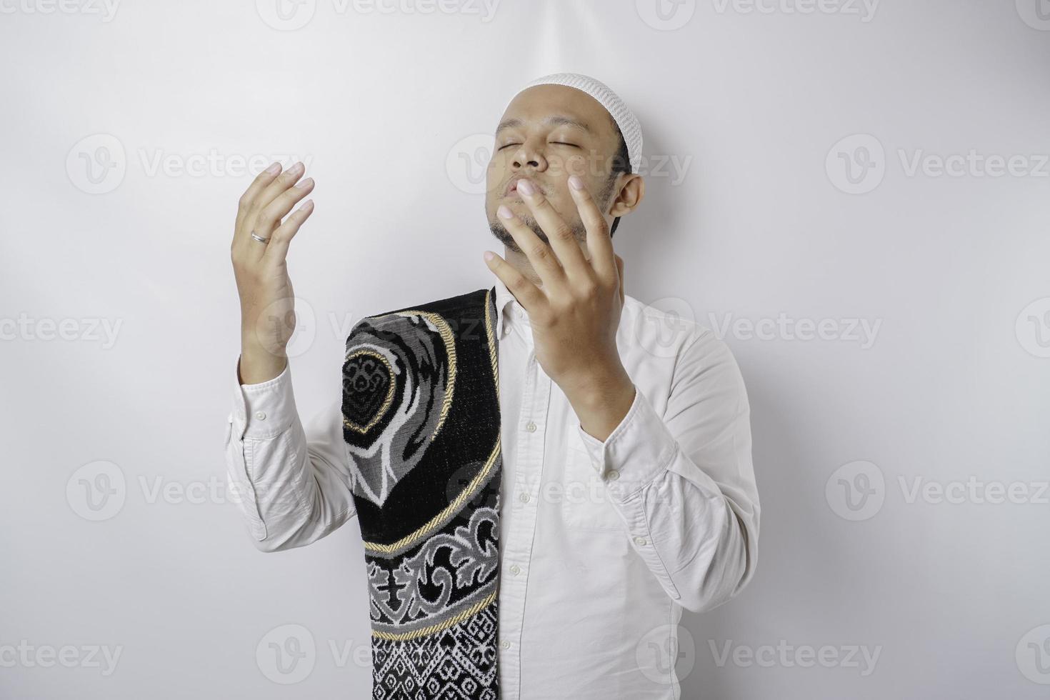 Happy handsome Asian Muslim man with prayer rug on his shoulder is praying to God. photo
