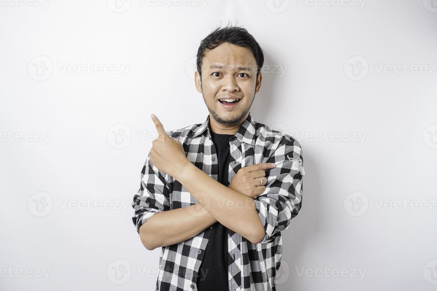 un hombre asiático sonriente con pantalones de tartán apunta al espacio de copia encima de él, aislado por fondo blanco foto