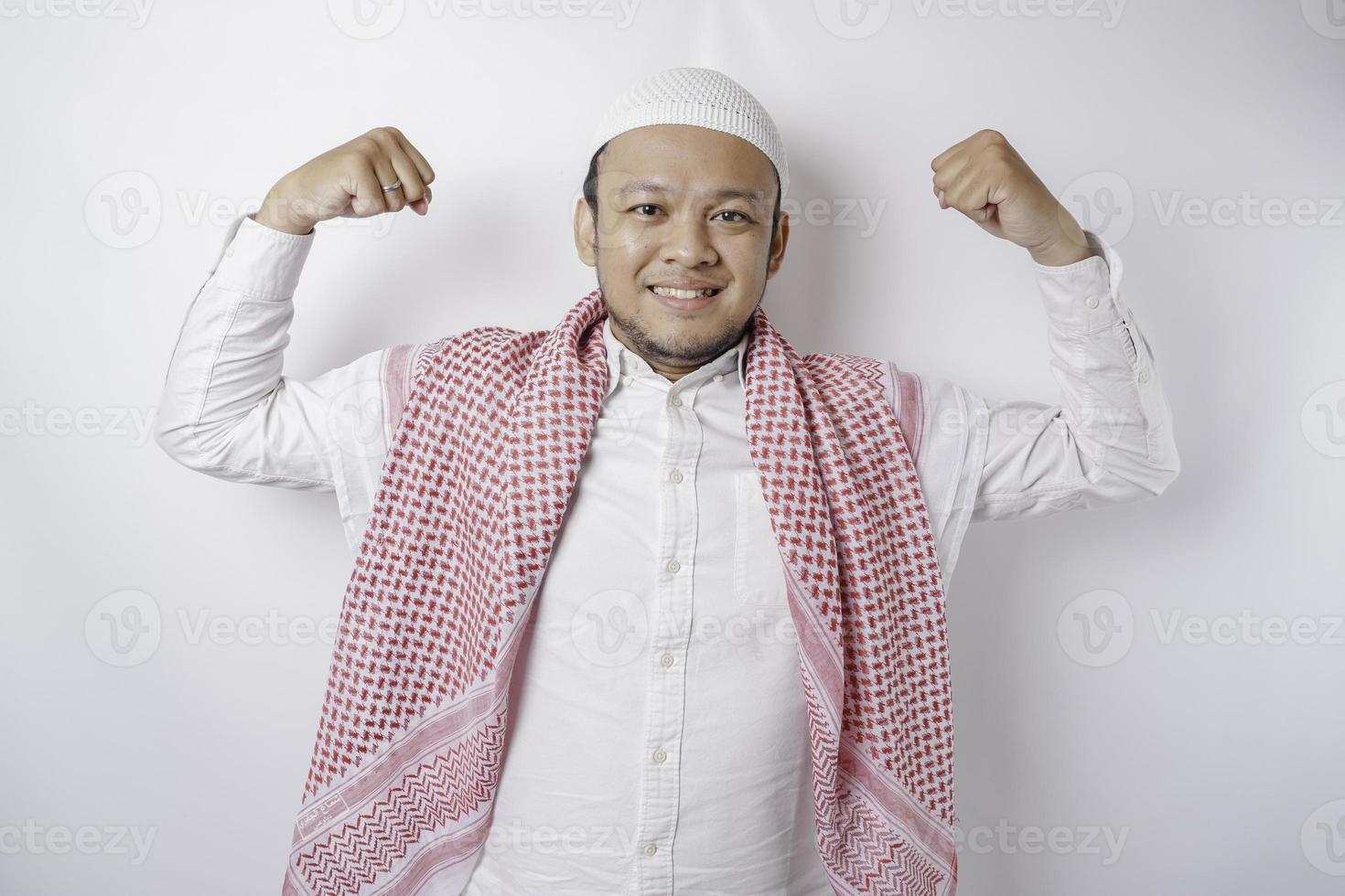 Excited Asian Muslim man showing strong gesture by lifting his arms and muscles smiling proudly photo