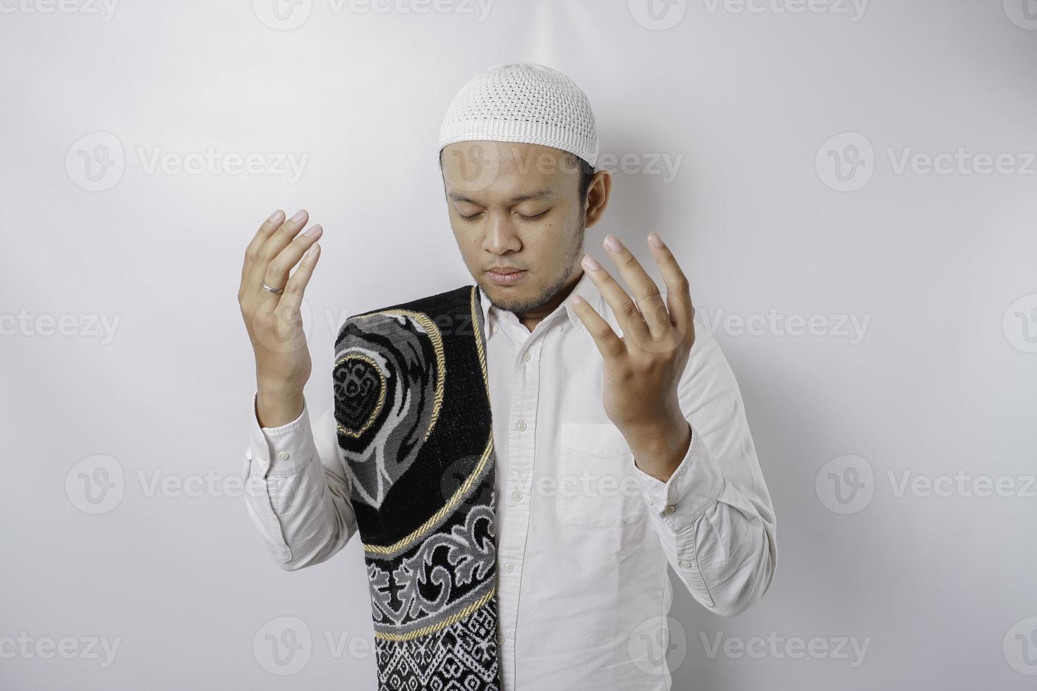 Happy handsome Asian Muslim man with prayer rug on his shoulder is praying to God. photo