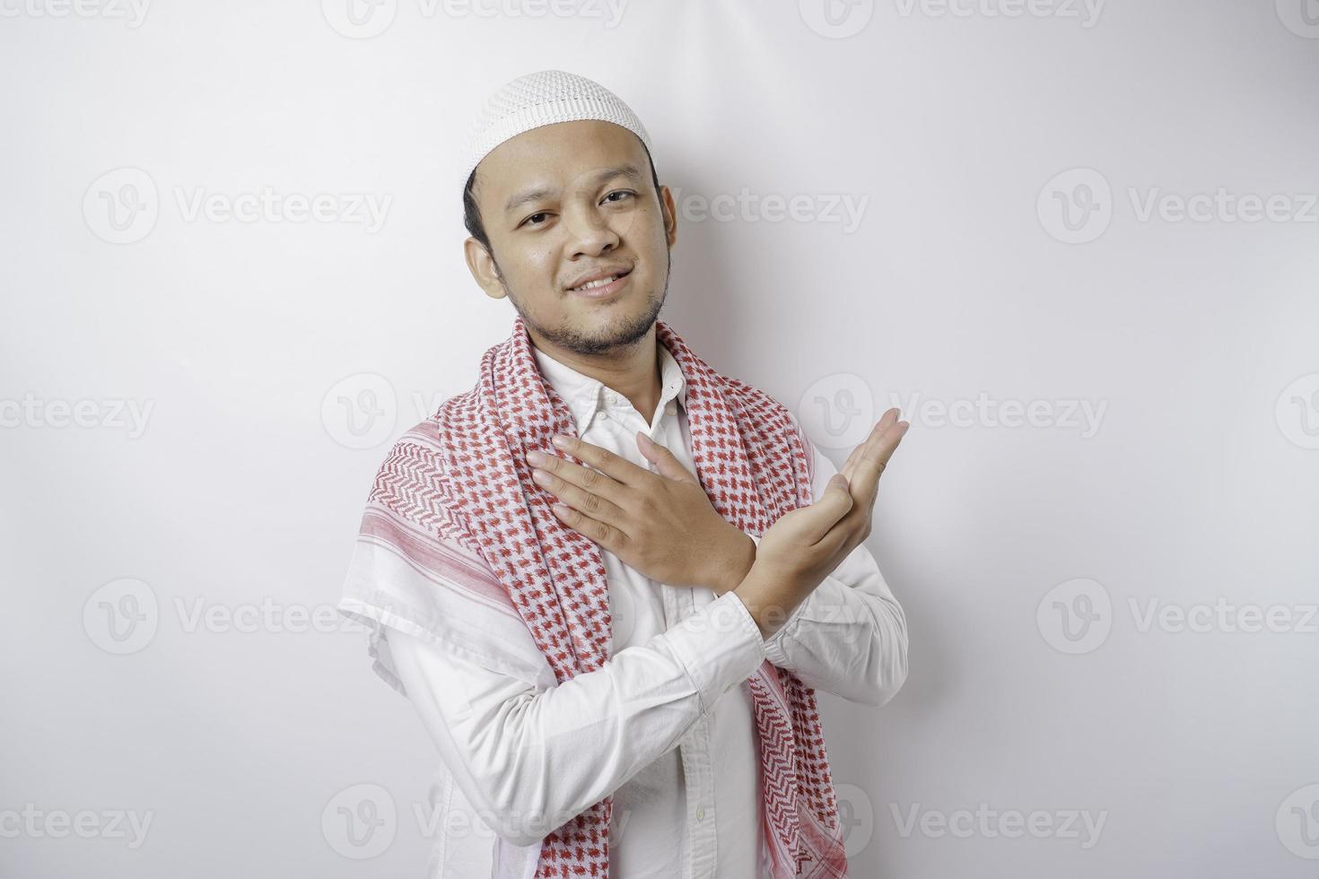 Smiling Asian Muslim man pointing at the copy space on top of him, isolated by white background photo