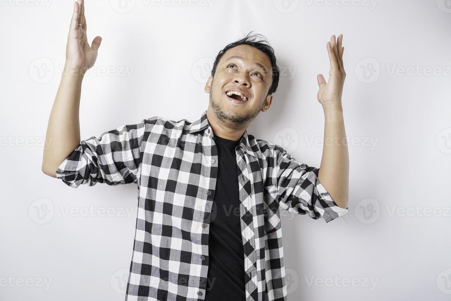Smiling Asian man wearing tartan shirt is pointing at the copy space on top of him, isolated by white background photo