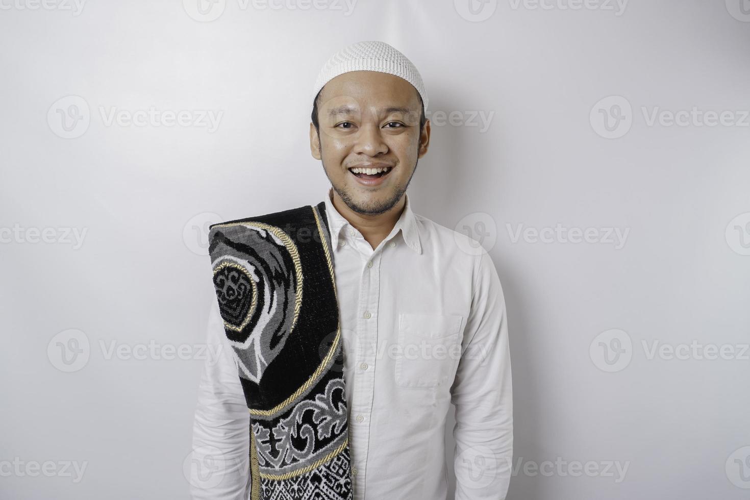 A portrait of a happy Asian Muslim man with prayer rug on his shoulder is smiling isolated by white background photo
