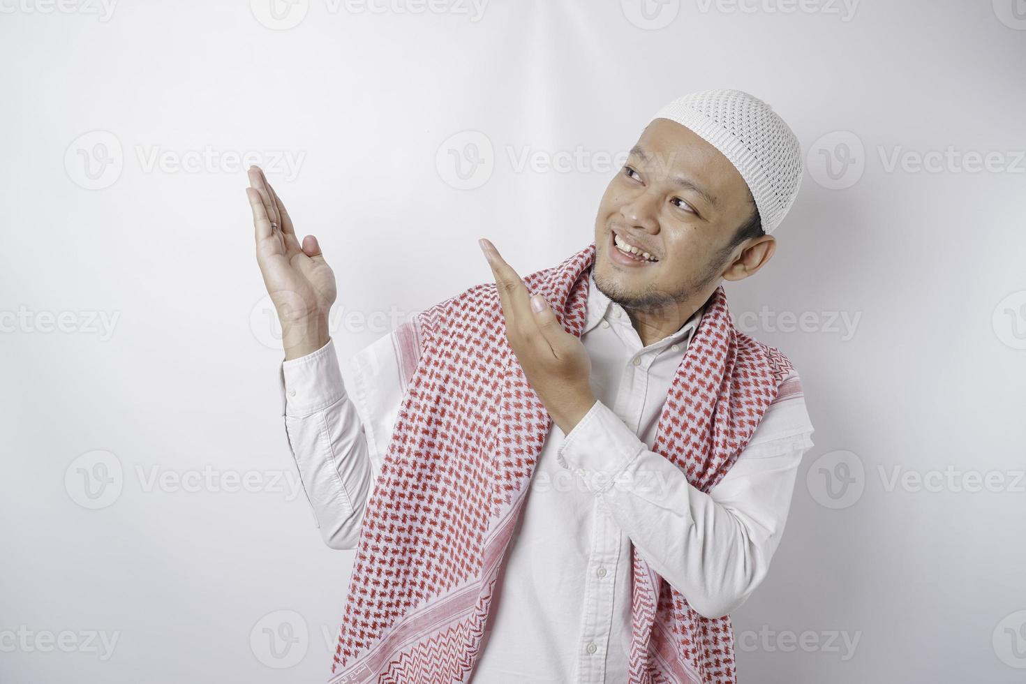 Excited Asian Muslim man pointing at the copy space beside him, isolated by white background photo