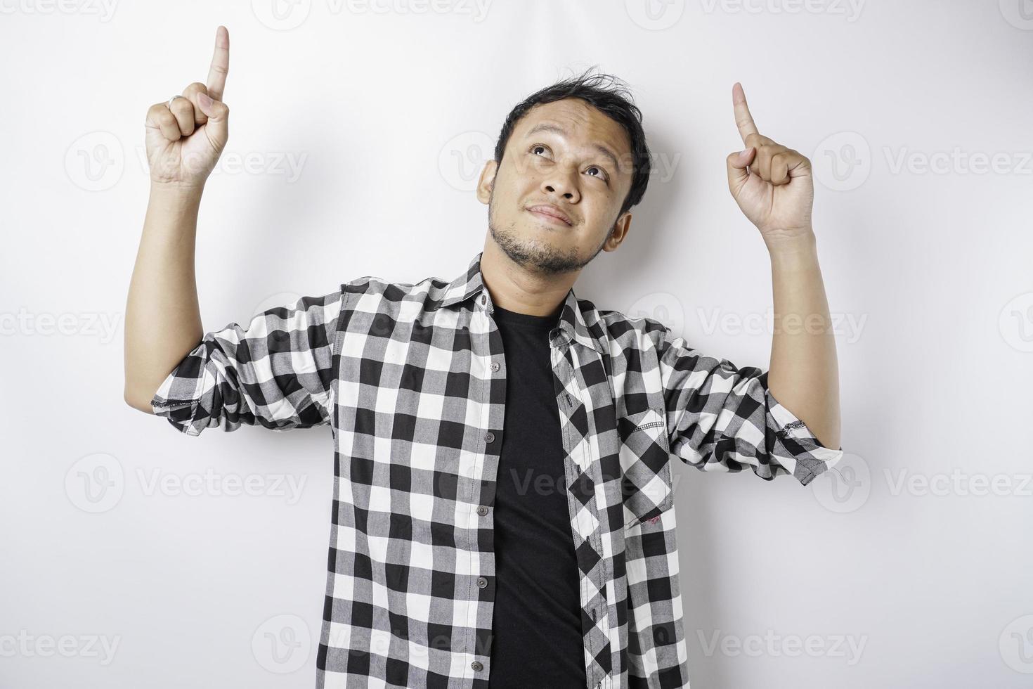 Smiling Asian man wearing tartan shirt is pointing at the copy space on top of him, isolated by white background photo