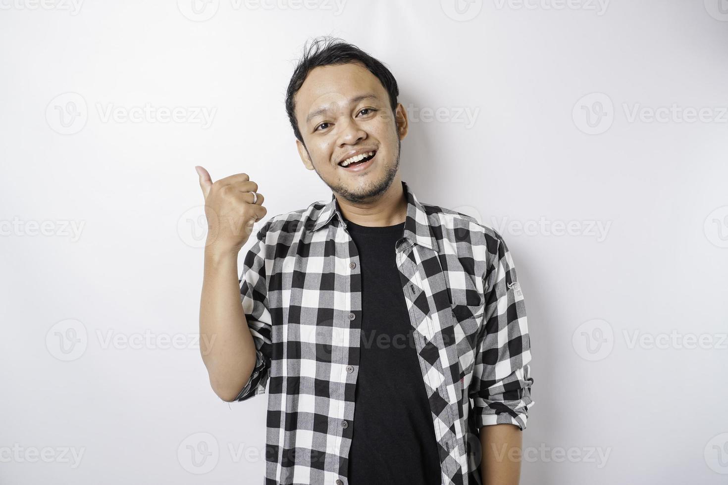 Excited Asian man wearing tartan shirt gives thumbs up hand gesture of approval, isolated by white background photo