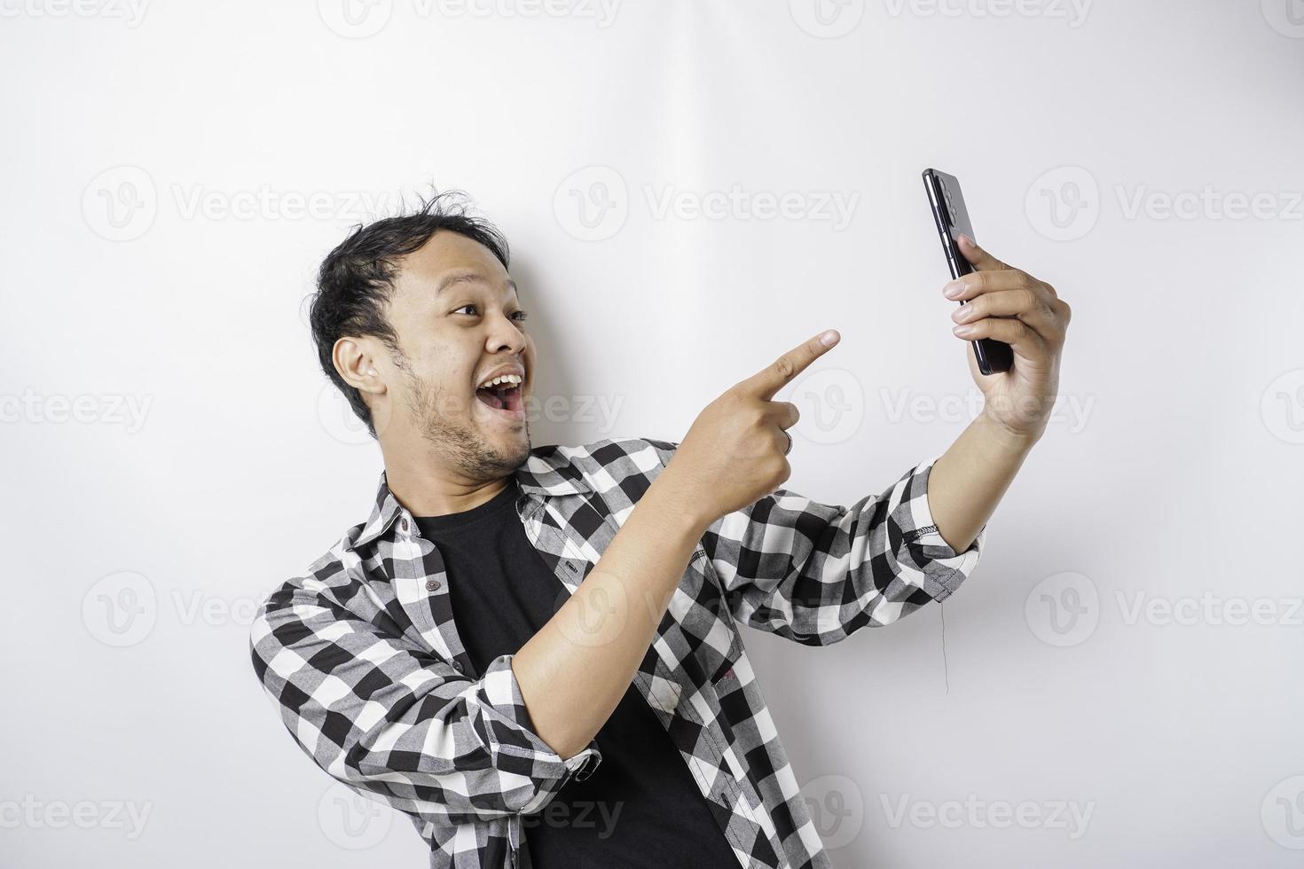 un retrato de un hombre asiático feliz sonríe mientras sostiene su teléfono, aislado por fondo blanco foto