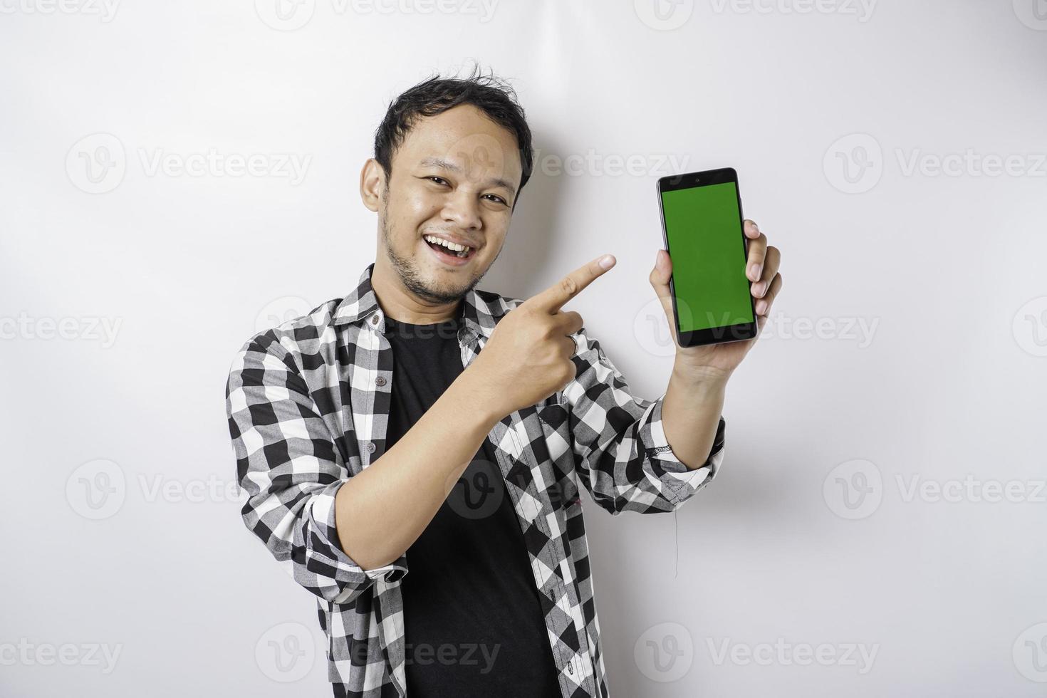 A portrait of a happy Asian man is smiling while showing copy space on his phone, isolated by white background photo