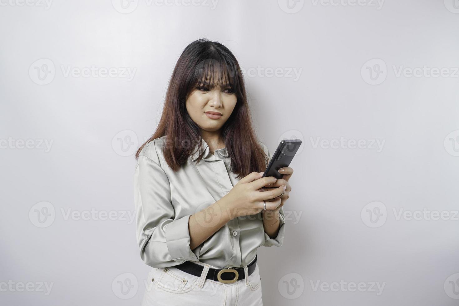una joven asiática insatisfecha se ve descontenta usando una camisa verde salvia expresiones faciales irritadas sosteniendo su teléfono foto