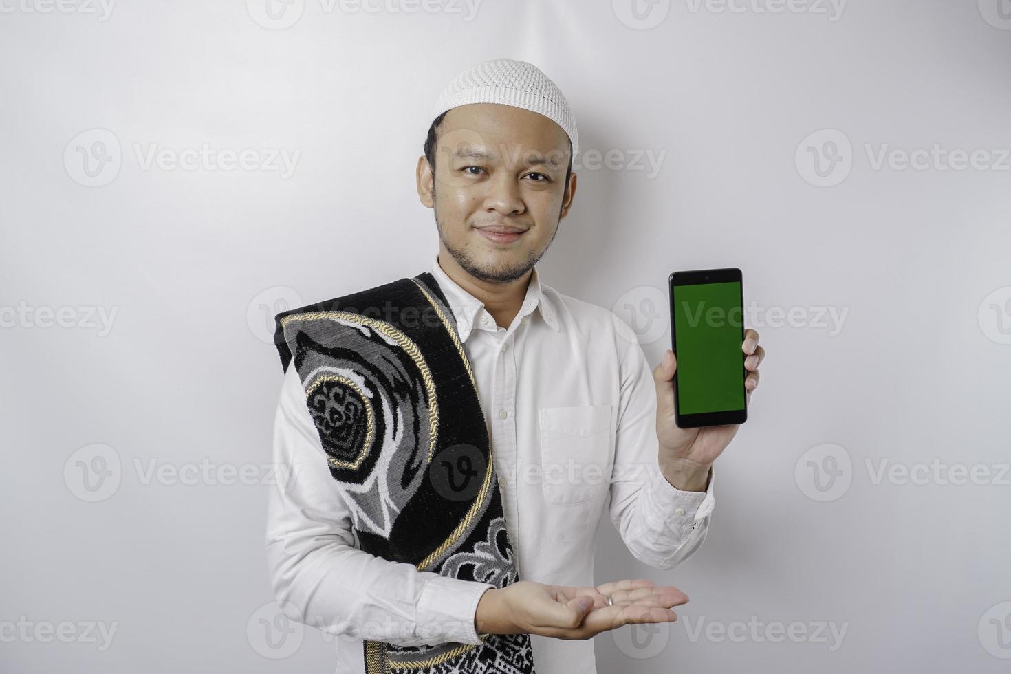un retrato de un musulmán asiático feliz sonriendo mientras muestra espacio de copia en su teléfono, aislado por fondo blanco foto