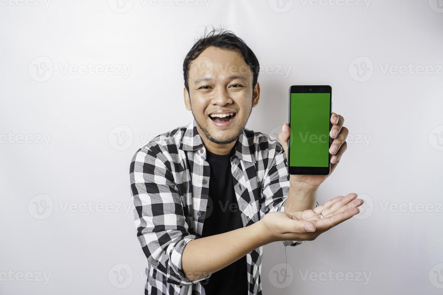 A portrait of a happy Asian man is smiling while showing copy space on his phone, isolated by white background photo