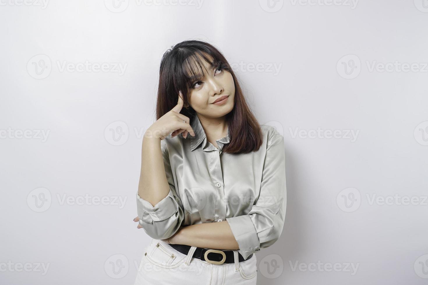 A thoughtful young woman is wearing sage green shirt and holding her chin isolated by white background photo