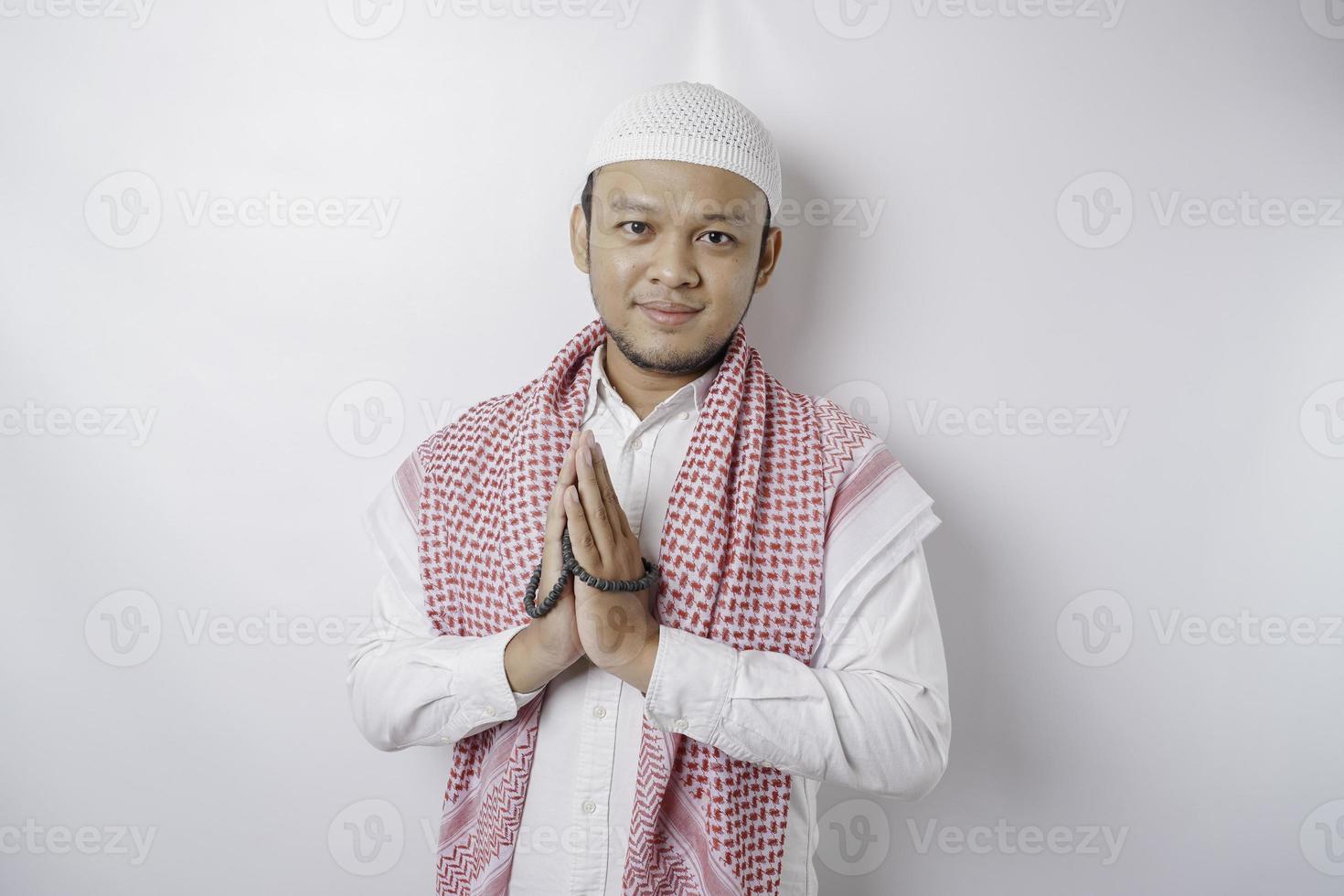 Sonriente joven musulmán asiático, gesticulando saludo tradicional aislado sobre fondo blanco. foto