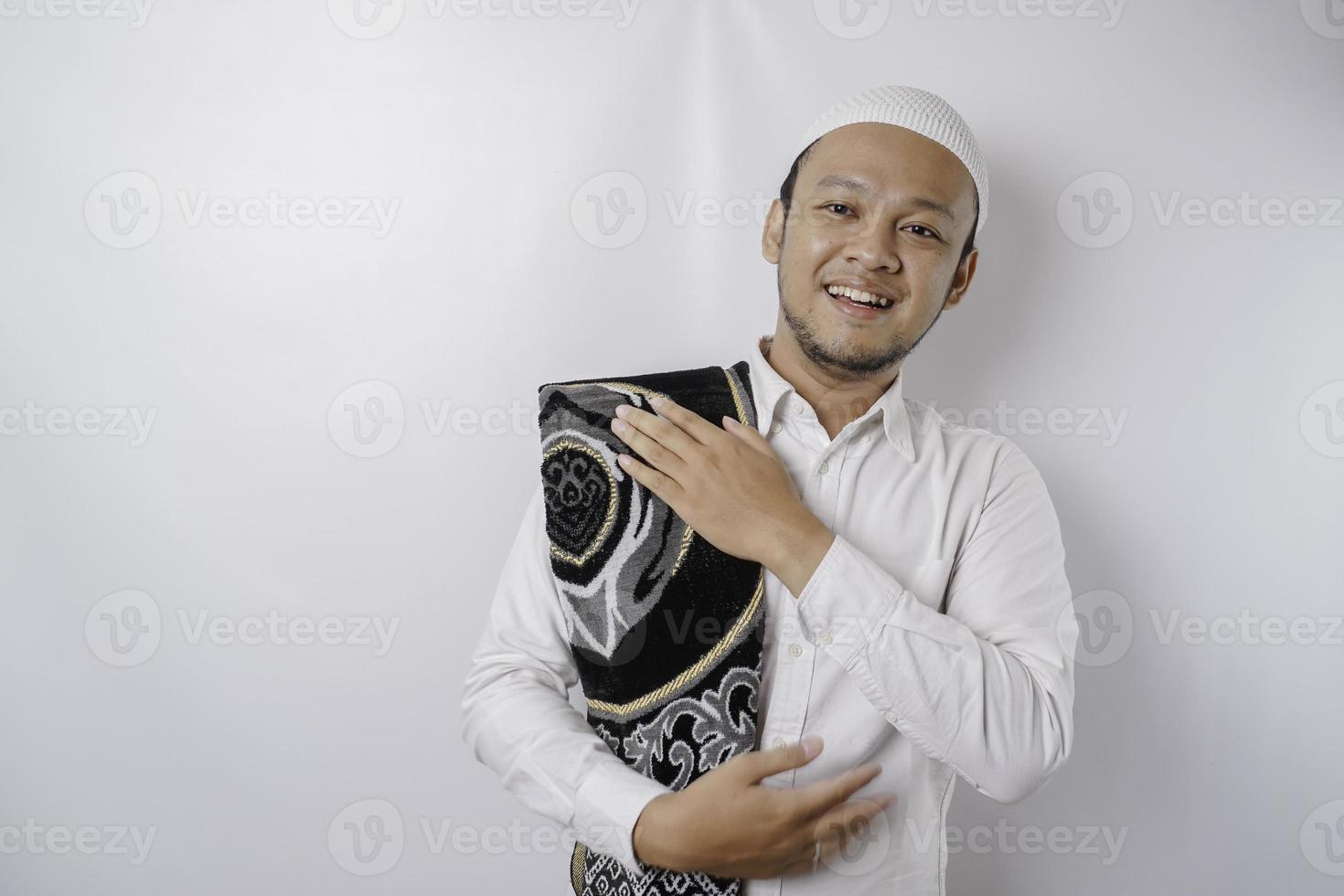 A portrait of a happy Asian Muslim man with prayer rug on his shoulder is smiling isolated by white background photo