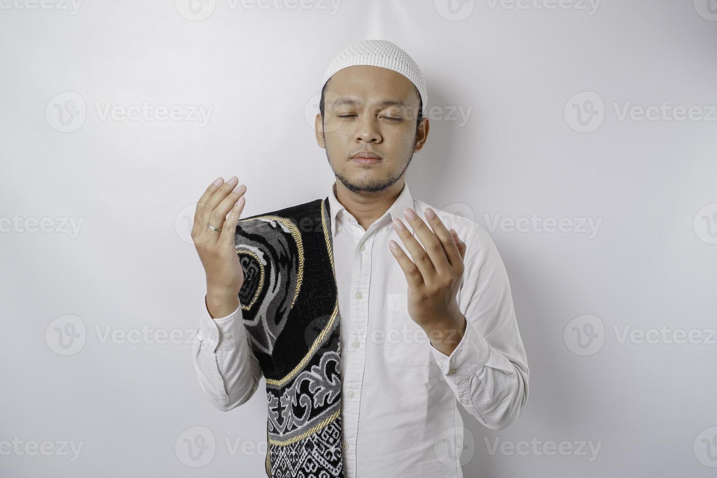 Happy handsome Asian Muslim man with prayer rug on his shoulder is praying to God. photo