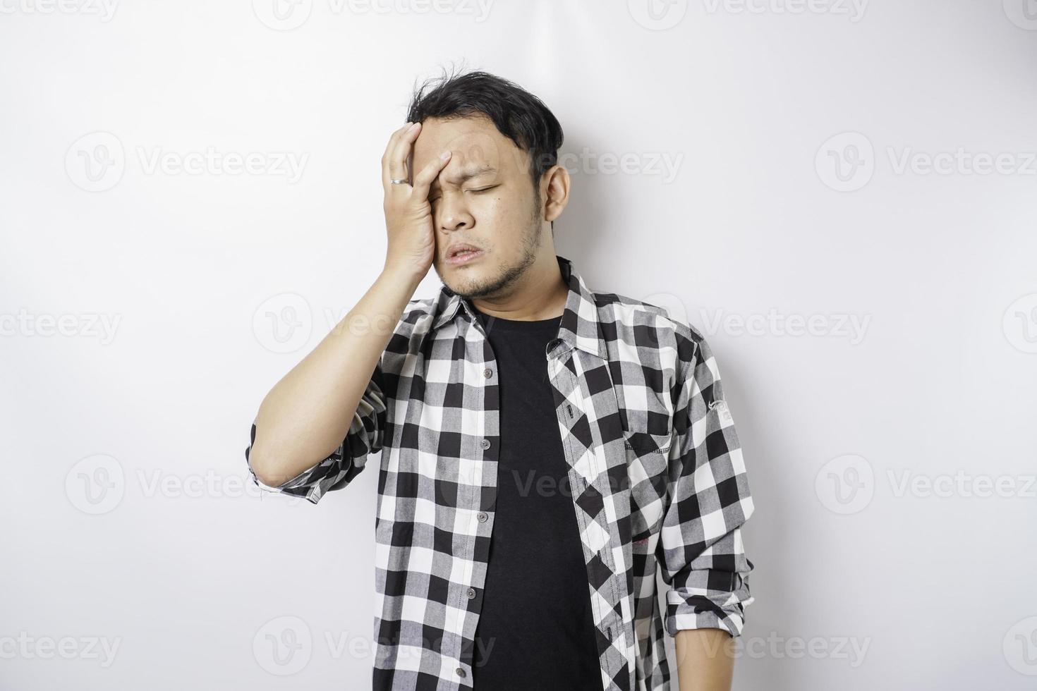 A portrait of a stressed Asian man wearing a tartan shirt isolated by white background looks depressed photo