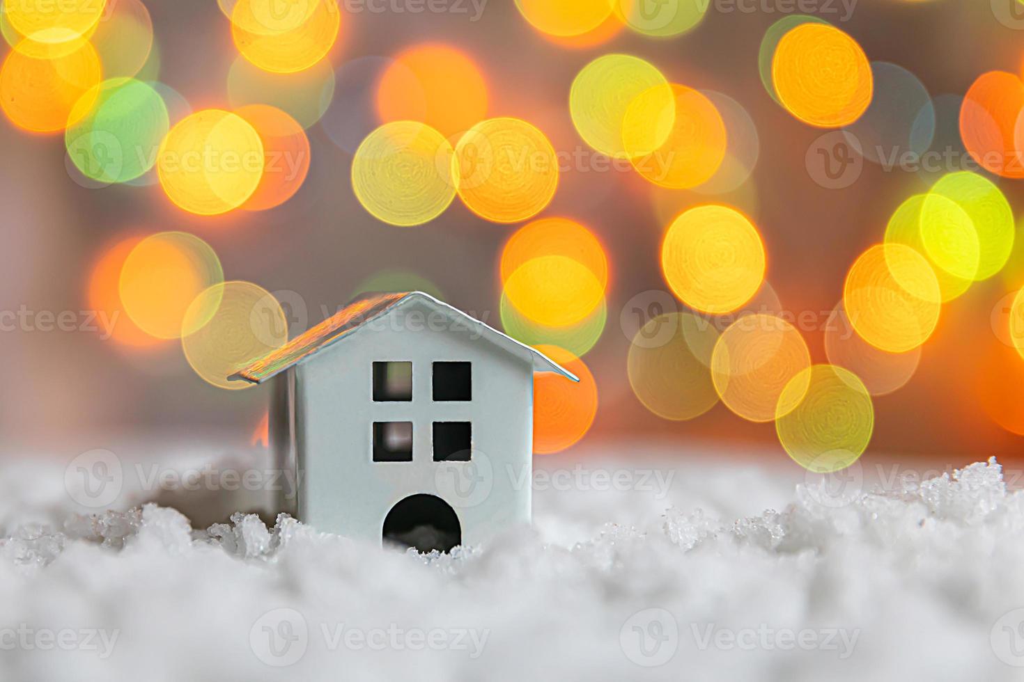 Abstract Advent Christmas Background. Toy model house on snow with defocused garland lights background. Christmas with family at home concept. Christmas winter composition. photo