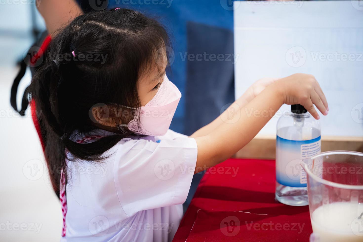 Portrait image girl 5-6 years old. Kindergarten child using alcohol gel for washing her hands, after learning art with classroom. Little kid wearing medical face mask to prevent dust PM2.5 and virus. photo