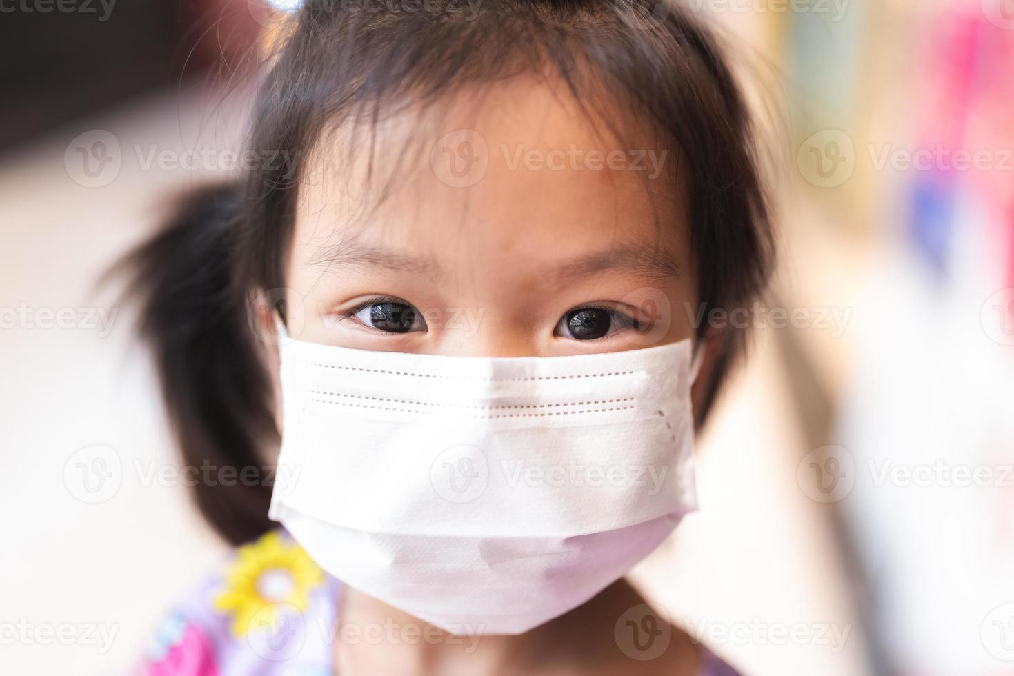 Closeup face kid girl wearing white medical mask. Prevent air pollution PM2.5 and virus. Child aged 5 years old. photo