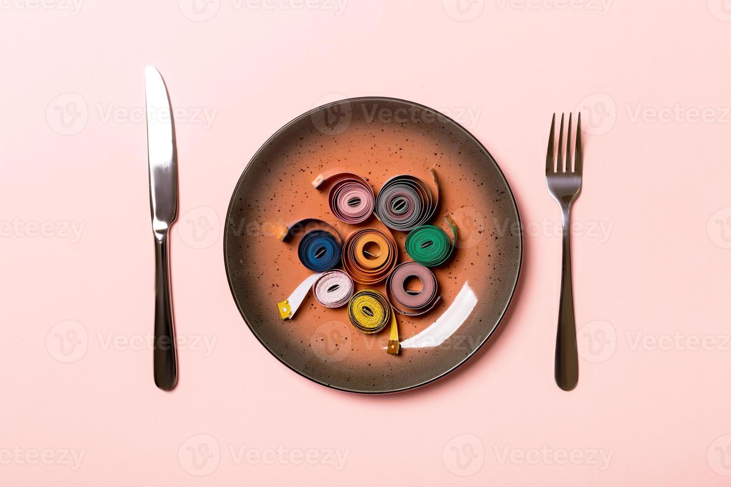 Healthy diet concept of plate with measuring tape, fork and knife on pink background. Top view photo