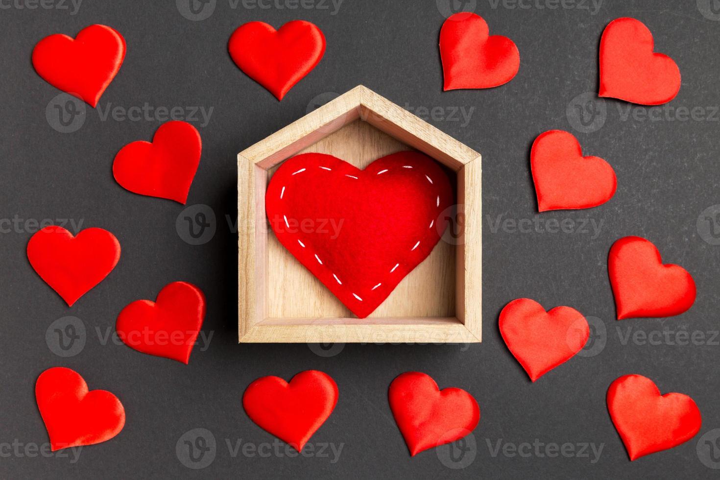 primer plano de corazón rojo en una casa de madera decorada con pequeños corazones sobre fondo colorido. día de San Valentín. concepto de hogar dulce hogar foto