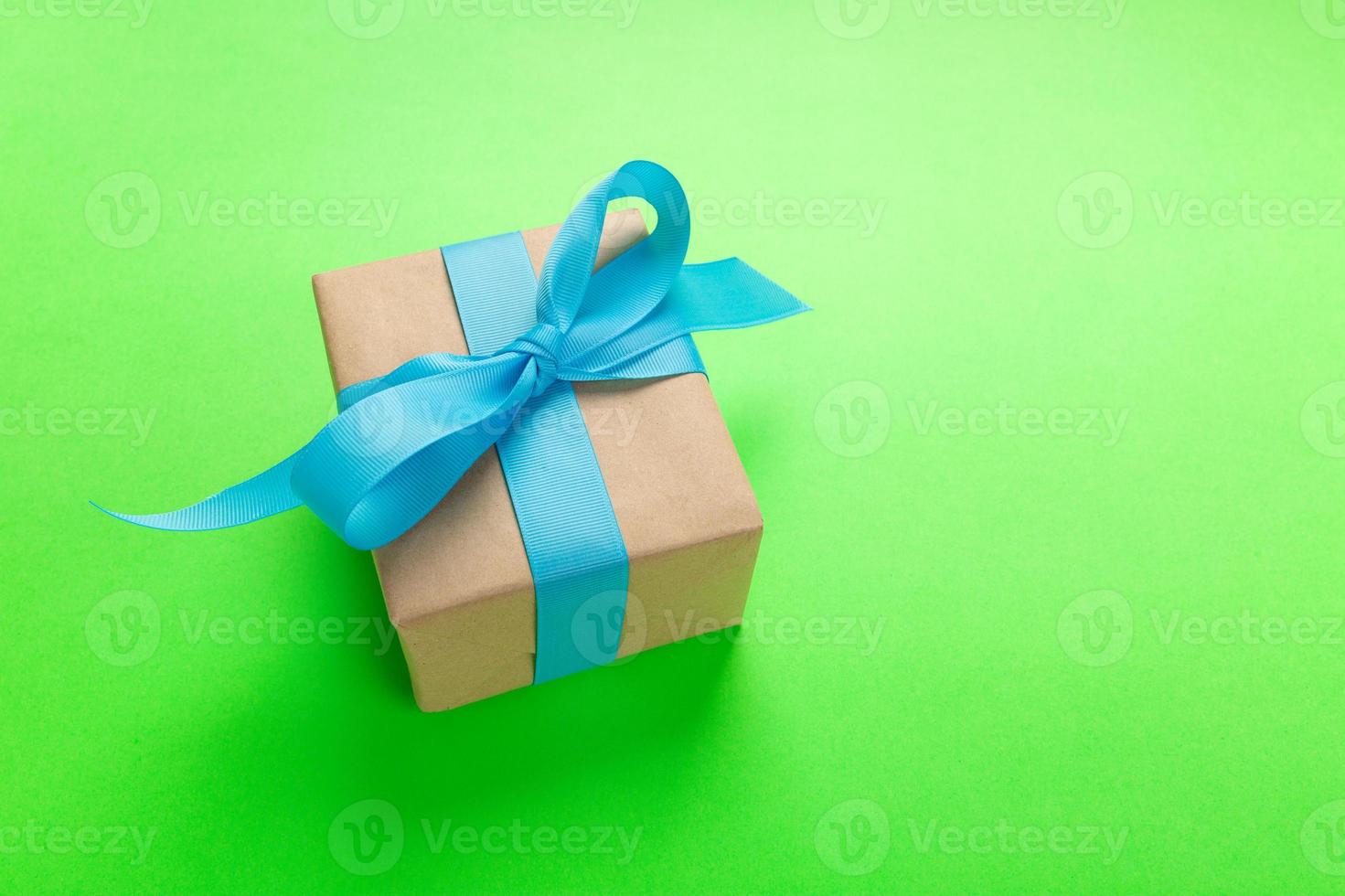 gift wrapped and decorated with blue bow on green background with copy space. Flat lay, top view photo