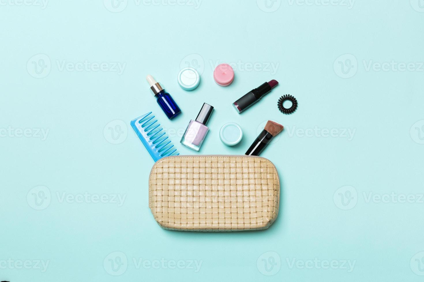 Top view of set of make up and skin care products spilling out of cosmetics bag on blue background. Beauty concept photo