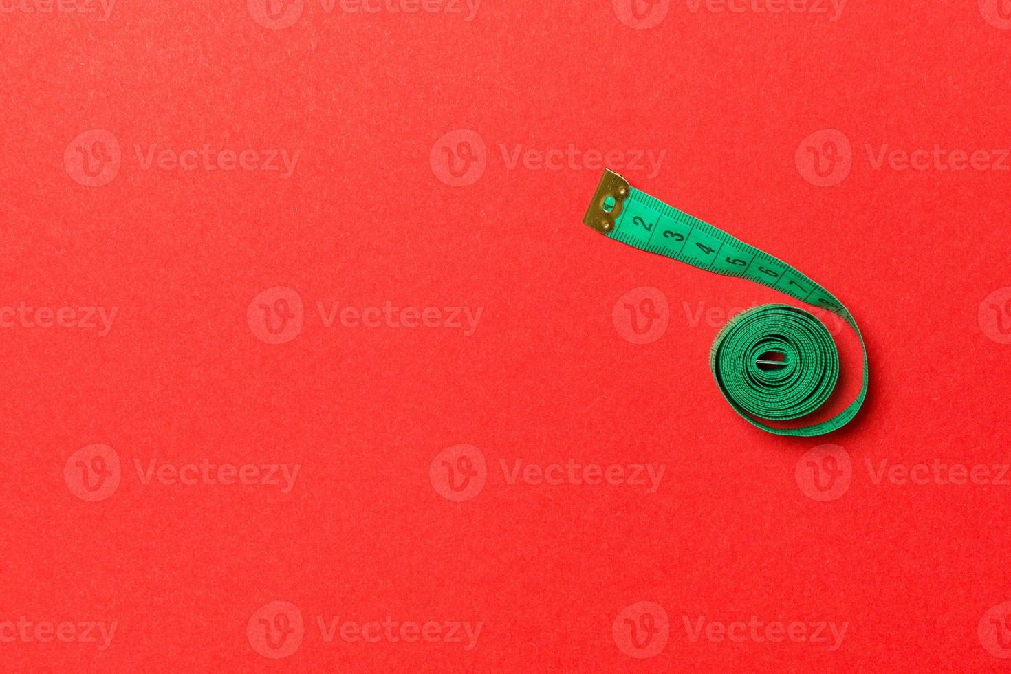 Top view of measure tape curtailed into a spiral with copy space. Concept of sewing accessory or healthy diet on red background photo