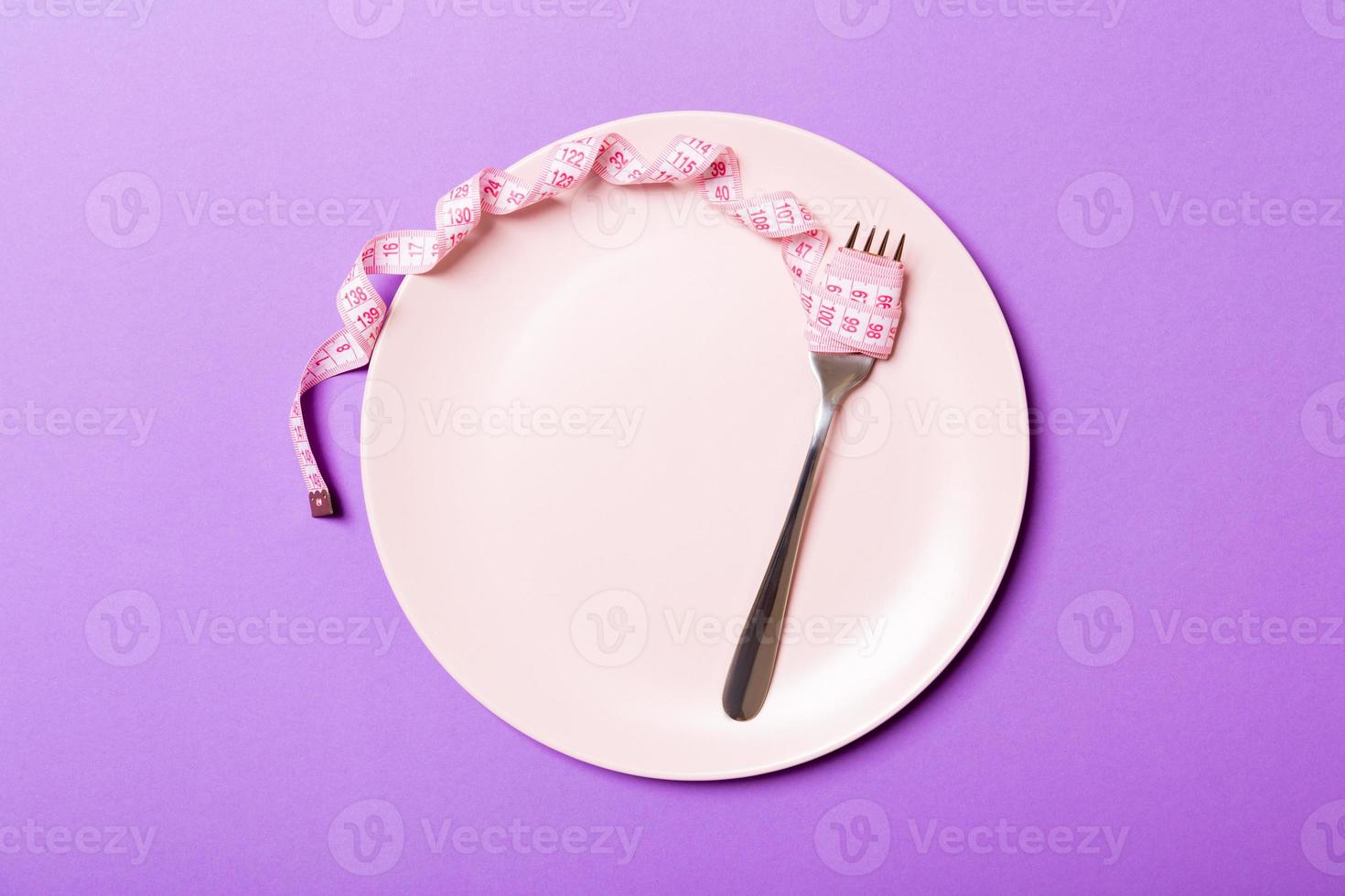 Strict diet concept with empty space fro your design. Top view of plate with fork in measuring tape on purple background photo