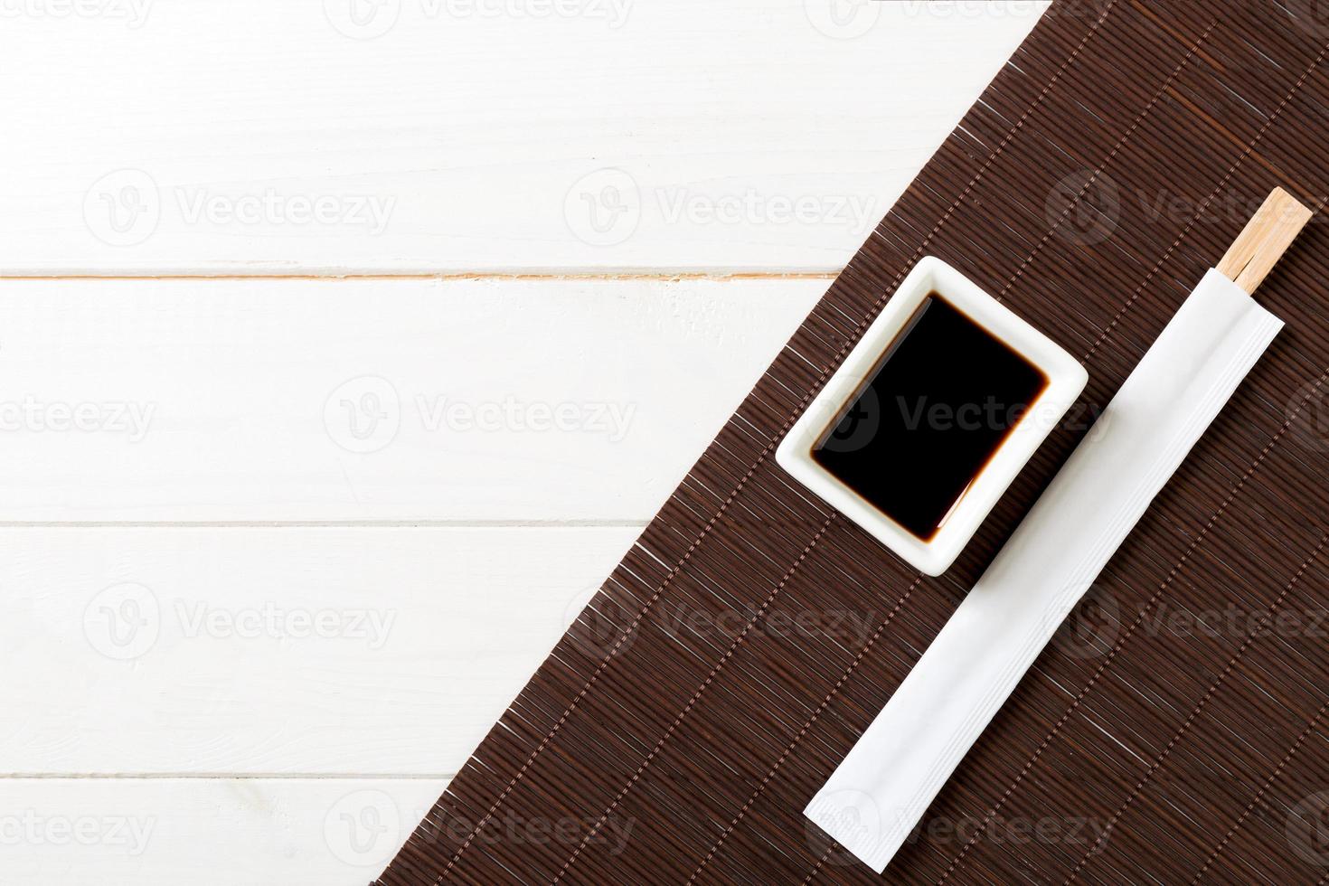 Bamboo mat and soy sauce with sushi chopsticks on white wooden table. Top view with copy space background for sushi. Flat lay photo