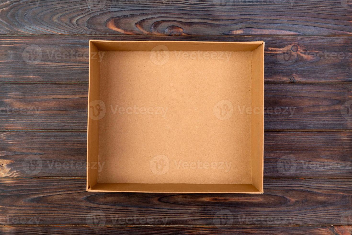 Opened brown blank cardboard box on wooden dark background, top view photo