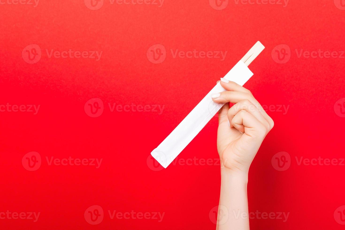 Woman's hand holding chopsticks in a pack on red background. Chinese food concept with empty space for your design photo