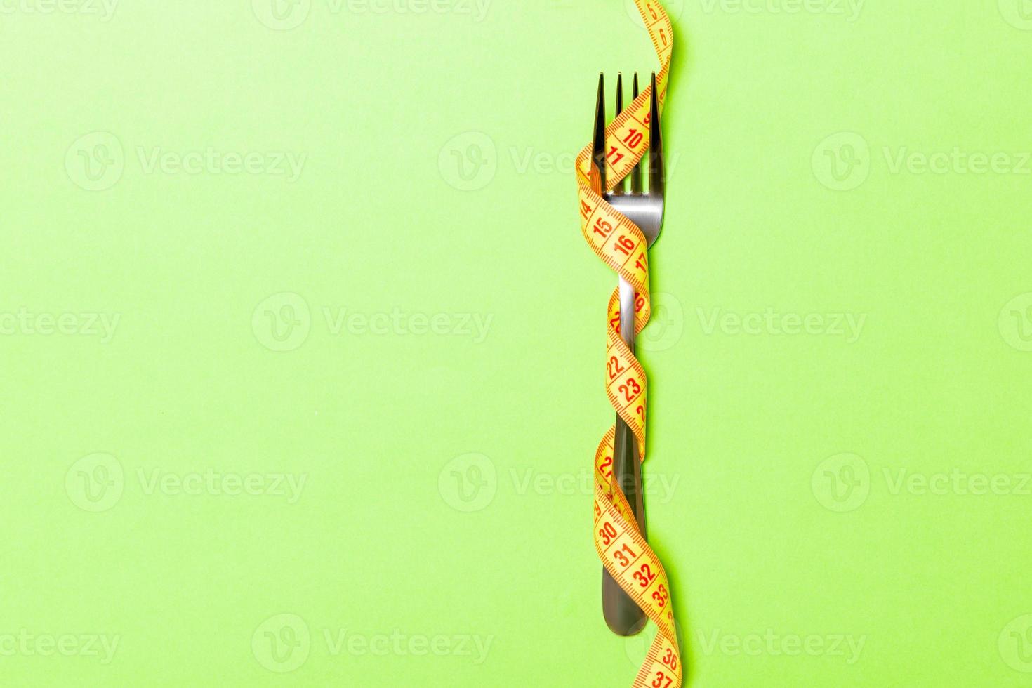 Fork wrapped in measuring tape on green background. Top view of overeating concept photo