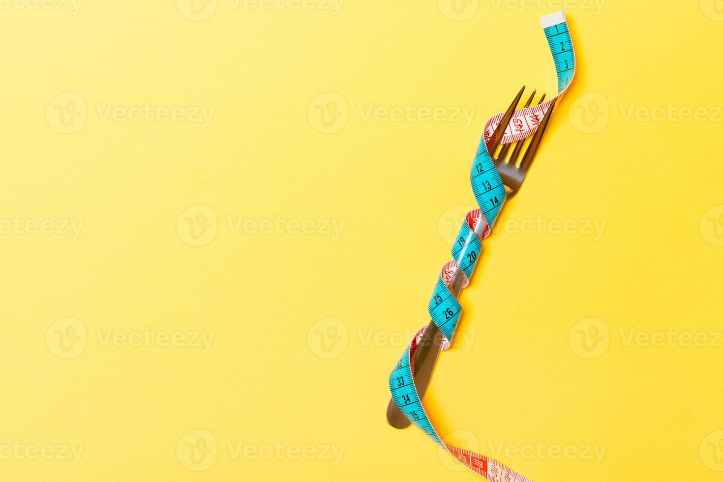 Diet and healthy eating concept with wrapped fork in measuring tape on yellow background. Top view of weightloss with copy space photo