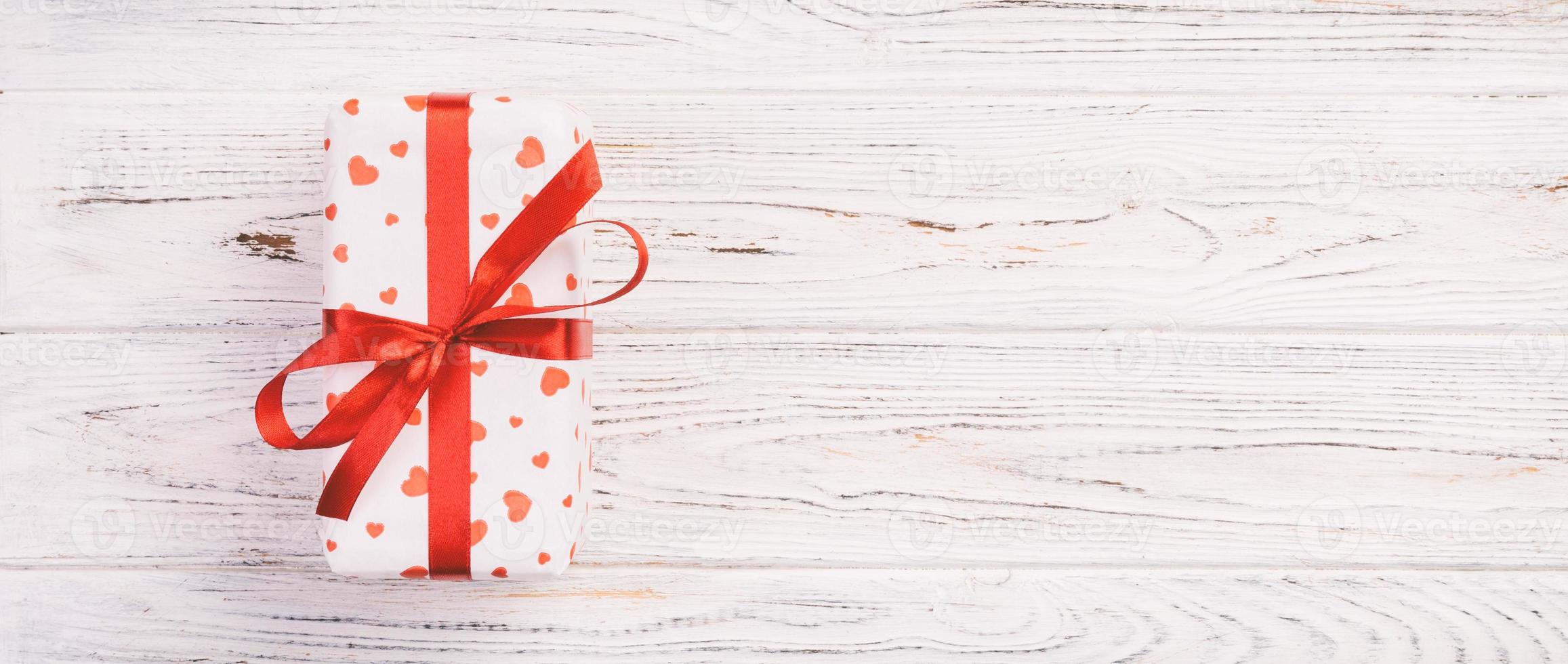 Valentine or other holiday handmade present in paper with red hearts and gifts box in holiday wrapper. Present box of gift on white wooden table top view with copy space, empty space for design photo