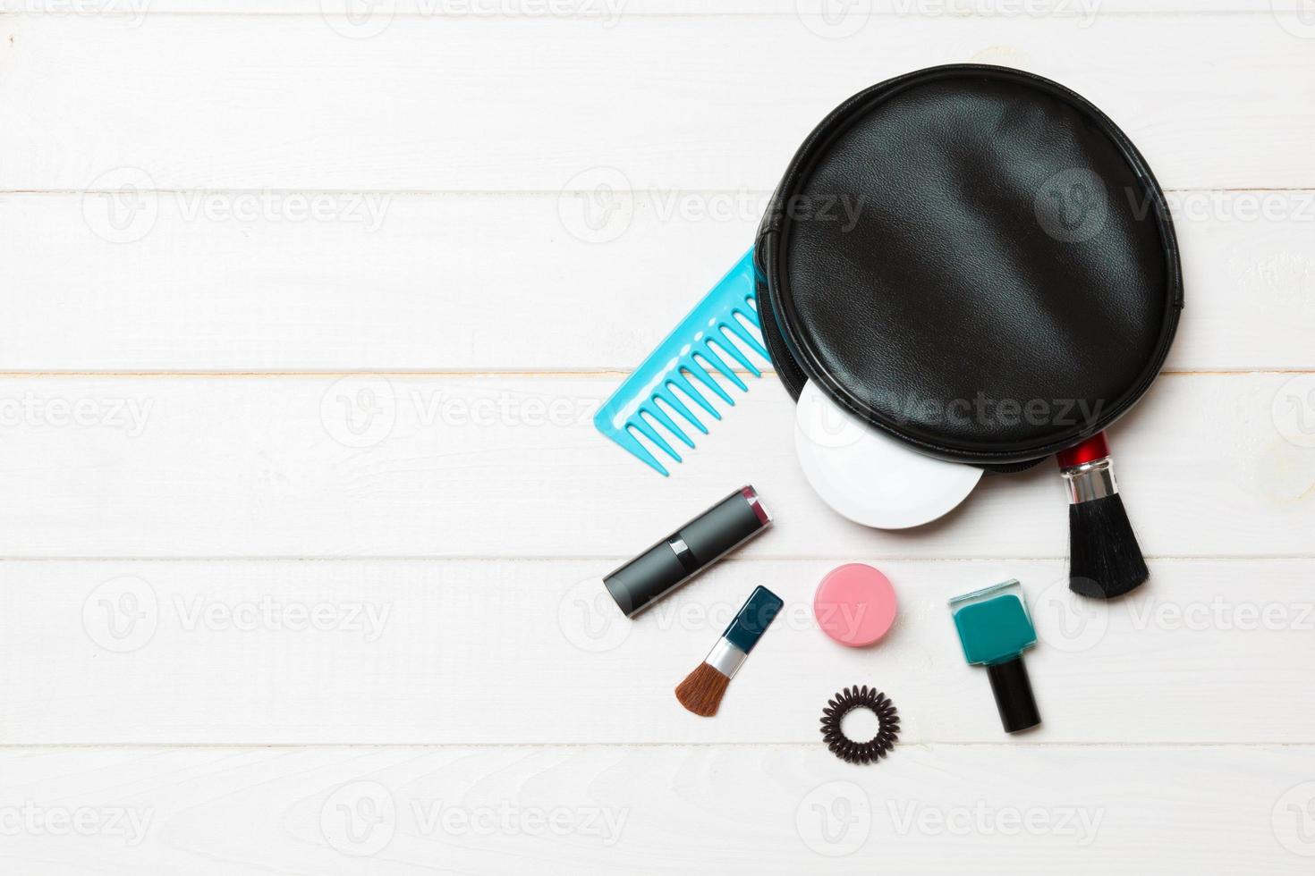 Aerial view of a leather cosmetics bag with make up beauty products spilling out on wooden background. Beautiful skin concept with copy space photo