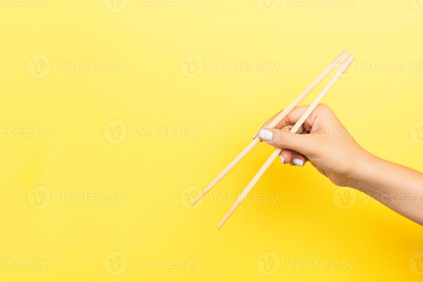 Girl's hand showing chopsticks on yellow background. Asian cuisine concept with empty space for your design photo
