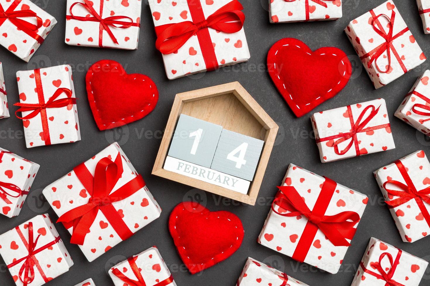 composición de calendario de madera, cajas de regalo blancas de vacaciones y corazones textiles rojos sobre fondo colorido. catorce de febrero. concepto del día de san valentín foto