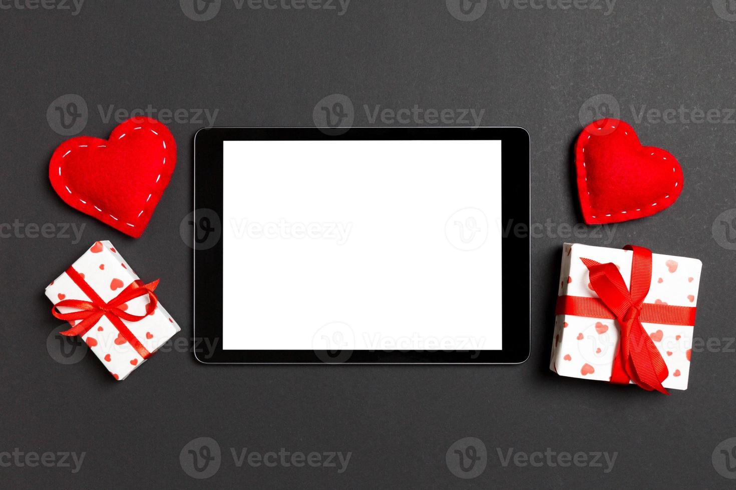 Top view of digital tablet surrounded with gift boxes and hearts on colorful background. Saint Valentine's day photo