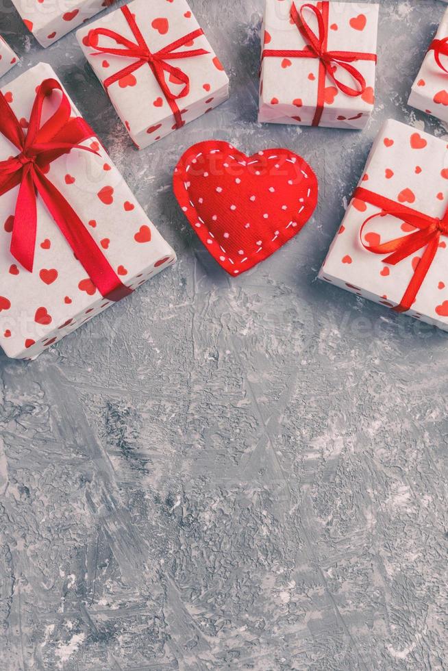 san valentín u otro regalo hecho a mano de vacaciones en papel con corazones rojos y caja de regalos en envoltorio de vacaciones. presente caja de regalo en la vista superior de la mesa de cemento gris con espacio de copia, espacio vacío para el diseño foto