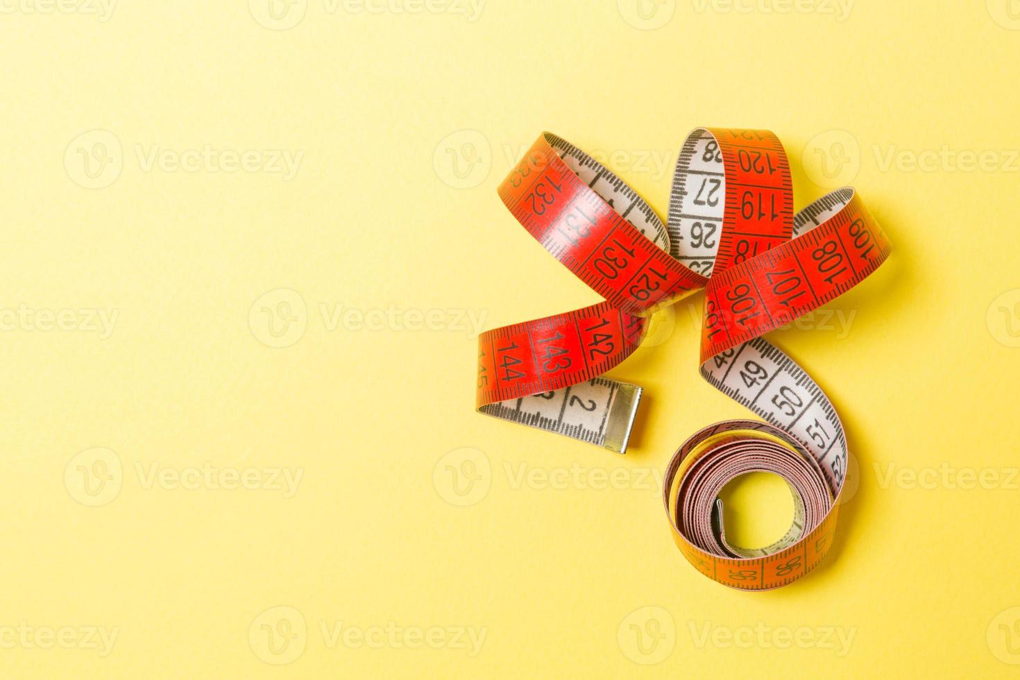 Top view of measure tape curtailed into a spiral with copy space. Concept of sewing accessory or healthy diet on yellow background photo